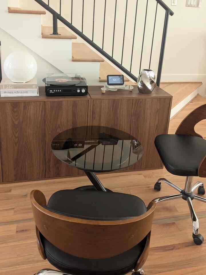 Natural wood and black toned home office featuring audio equipment on a sideboard and a round glass table with office chairs, modern interior