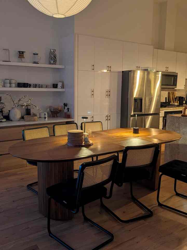 Warm brown wood tone dining room featuring a wooden dining table and rattan chairs illuminated by ambient pendant light in kitchen space