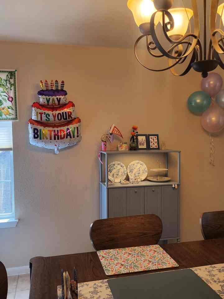 Beige-toned dining room featuring wooden dining table with floral placemats and birthday party decorations on the wall