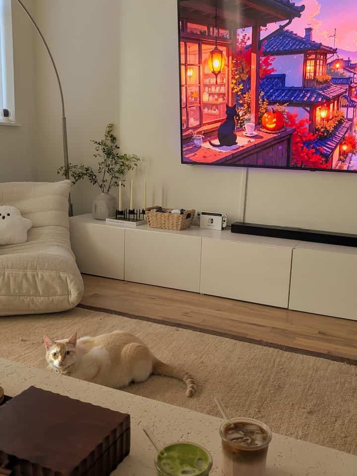 Beige and white toned living room featuring a large sofa, TV stand, floor rug, and coffee table creating a cozy home cafe atmosphere