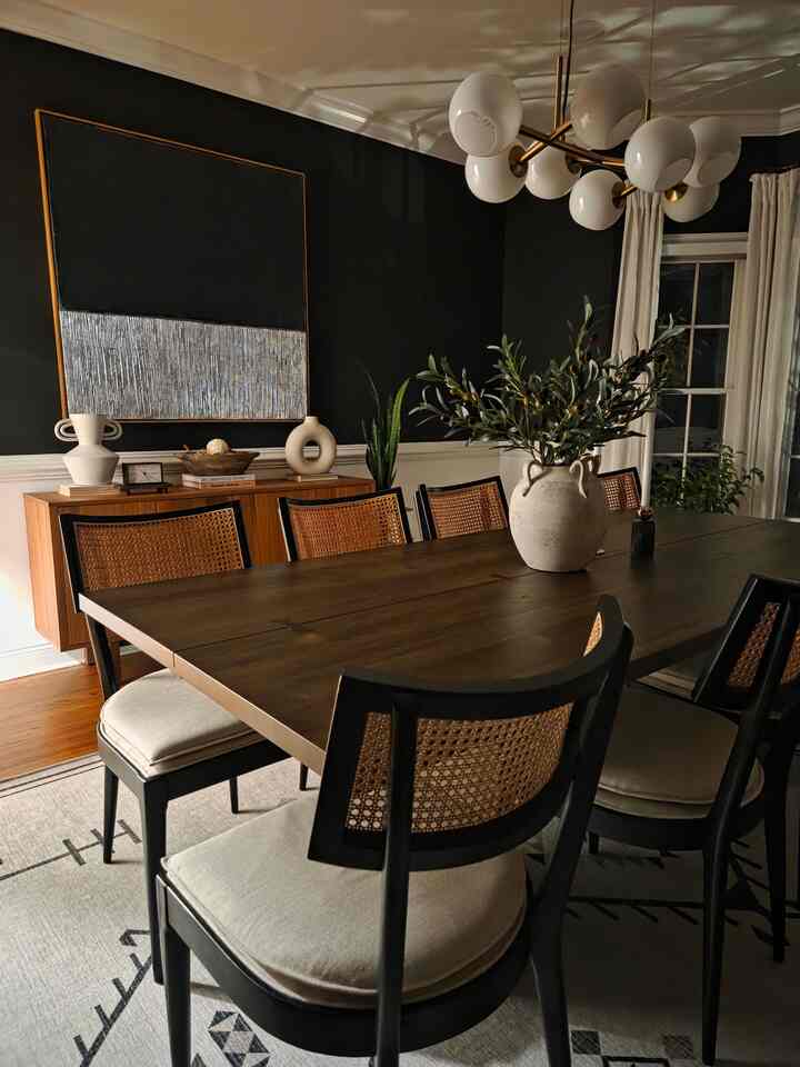 Cozy dining room with black walls and wood-tone dining table, featuring natural rattan chairs and a modern chandelier