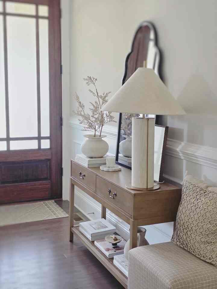 Warm beige and wood tone entrance featuring a simple console table, table lamp, and cushion creating a cozy atmosphere