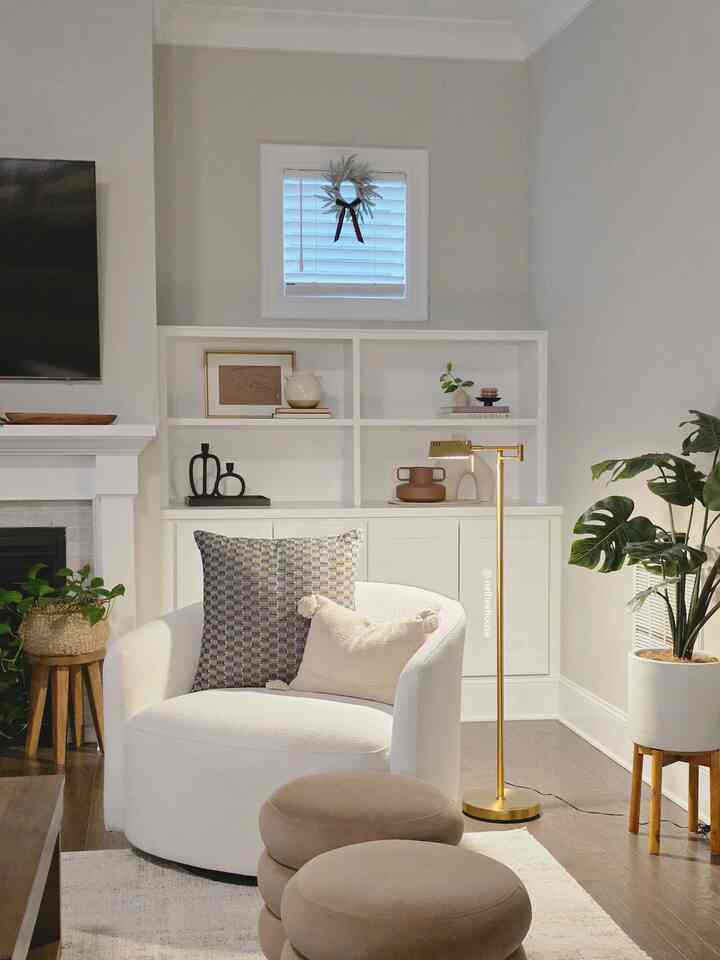 Warm beige and white toned living room corner featuring a cozy rounded armchair and gold floor lamp with simple, inviting atmosphere