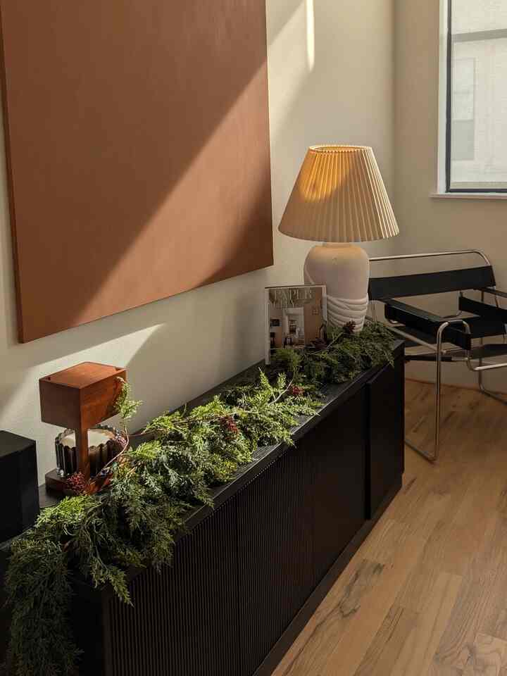 Natural color living room with brown wall panel and natural garland, featuring black sideboard and Wassily chair