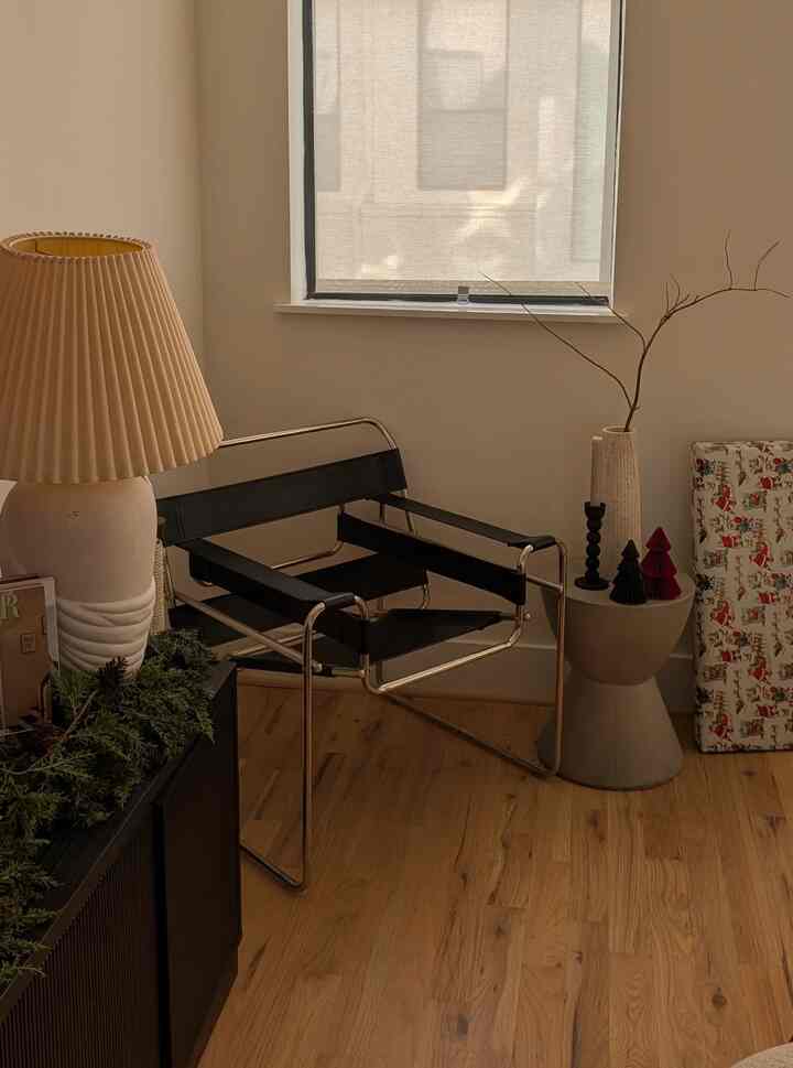 Soft beige and wood-tone corner living space featuring a black armchair and beige table lamp with a natural ambiance