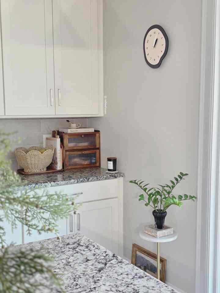 Modern kitchen with white cabinetry and natural tones, featuring a wall clock and green plant creating a cozy atmosphere
