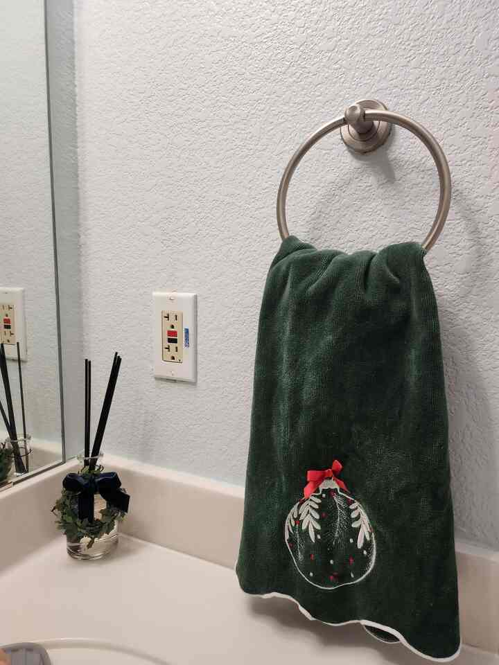 Light-toned bathroom featuring a green towel hanging on a ring and a diffuser on the sink counter with a clean atmosphere
