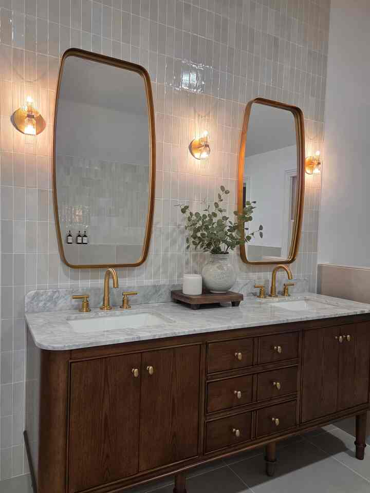 Modern classic bathroom featuring warm brown wood tone vanity, gold wall sconces, and large mirrors with marble countertop