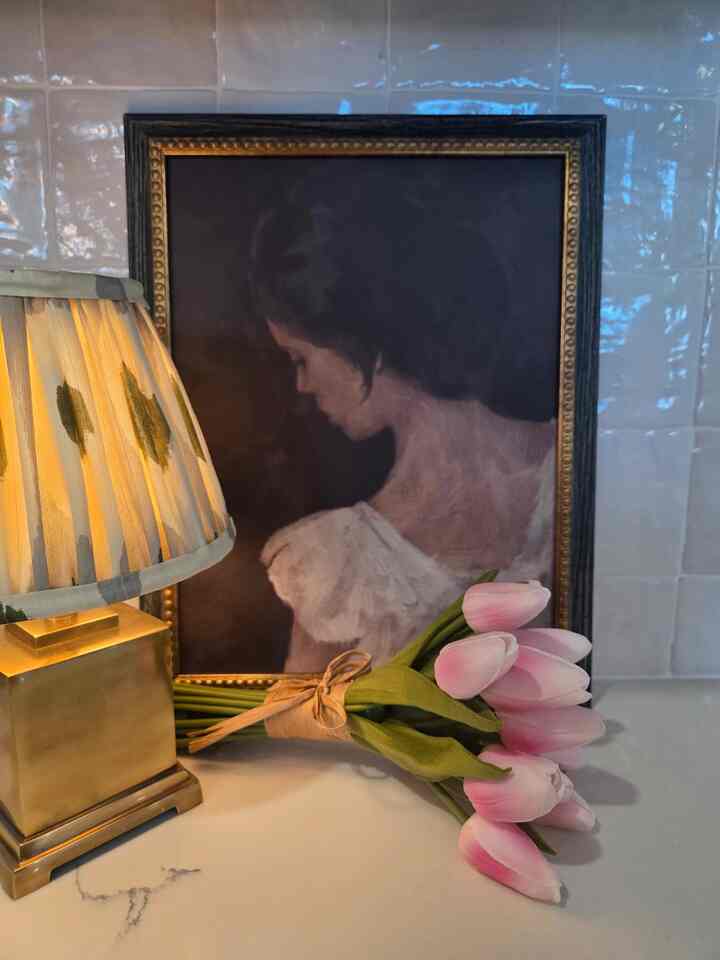 Cozy space featuring soft pink tulip bouquet and golden table lamp, with a female portrait wall art as backdrop creating a warm atmosphere