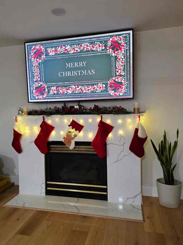 White-walled living room with wood tone flooring, cozy fireplace mantle decorated with Christmas garland and red stockings