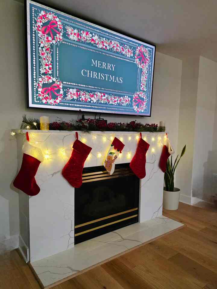 A bright and warm living room with white walls, red garland, Christmas stockings, and soft glowing string lights above the fireplace