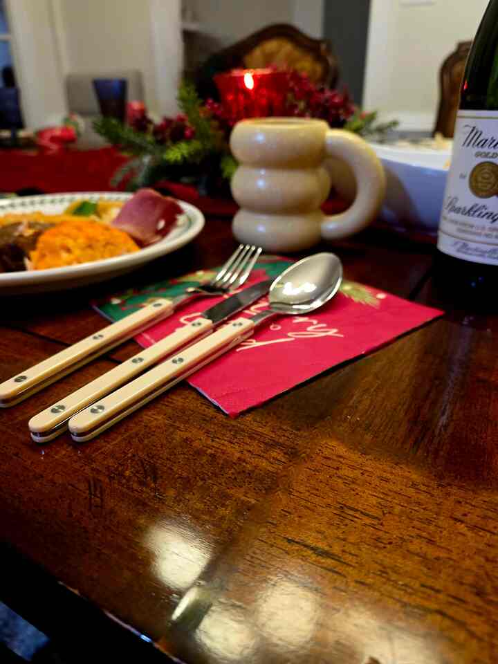 Warm brown wooden dining table featuring a beige mug and beige cutlery on a simple and cozy Christmas home party dinner setting
