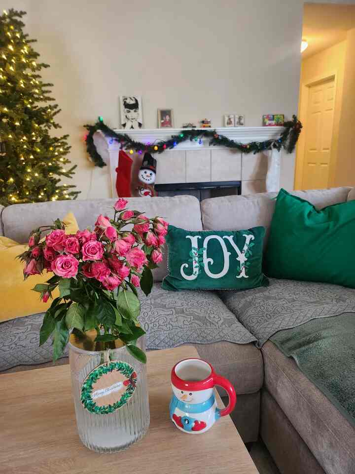 Living room with gray sofa and Christmas decorations, featuring a transparent glass vase with pink roses at the center