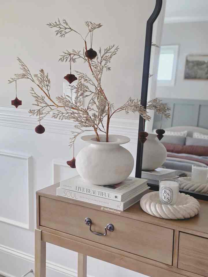 Natural-toned entrance space featuring a wood tone console table with neutral colored vase, dried flowers, and a candle creating a cozy ambiance