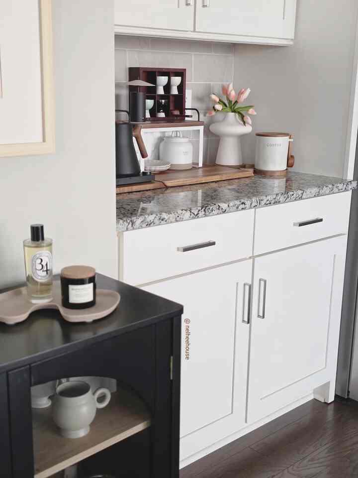Bright white-toned kitchen corner featuring wood-tone countertop, tulip vase, and coffee equipment in a cozy home cafe setup