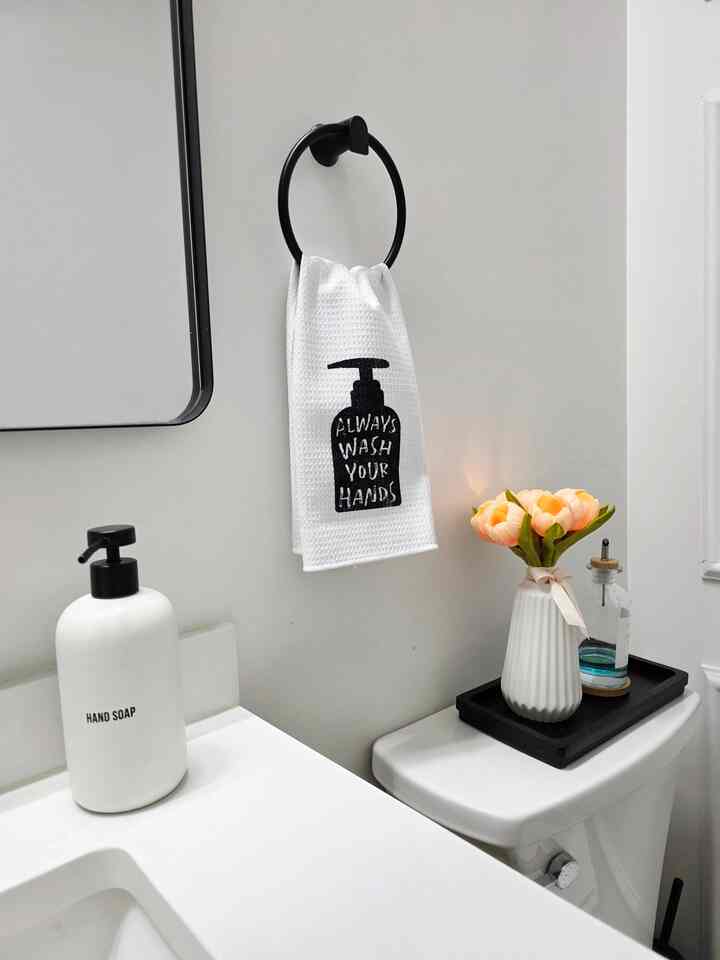 White-toned bathroom featuring sink countertop with hand soap, towel on black ring, and vase with flowers on toilet tank in a neat setting