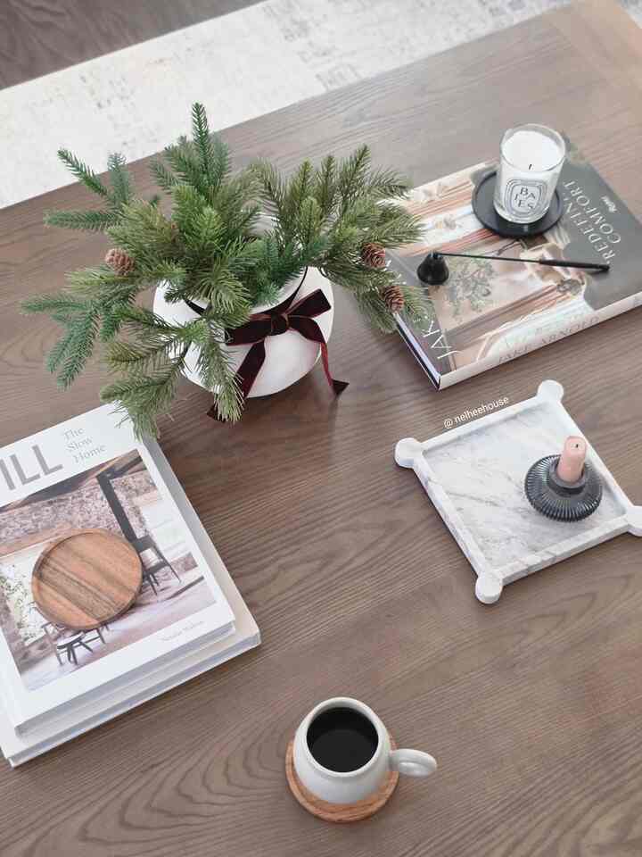 Wood tone coffee table featuring a plant, candles, books, and a mug, styled as a cozy home cafe in a living room space