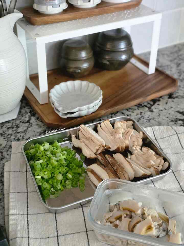 Natural toned kitchen featuring stainless steel tray with sliced green onions and mushrooms, wooden trays and ceramic dishes creating a calm atmosphere