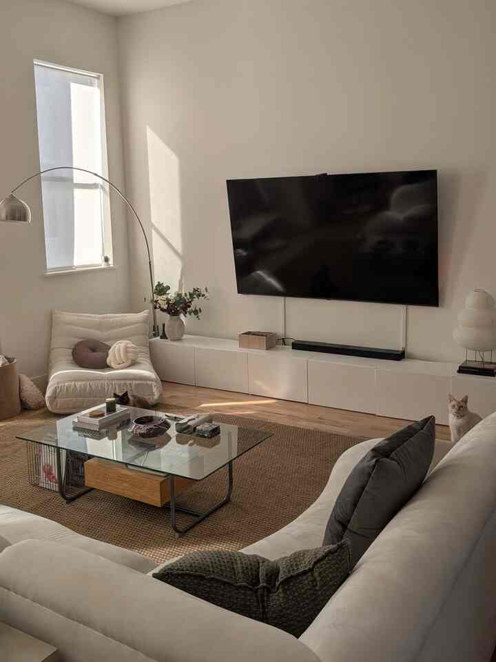 Living room in white and natural tones featuring a large sofa, wall-mounted TV, and two cats in a cozy atmosphere