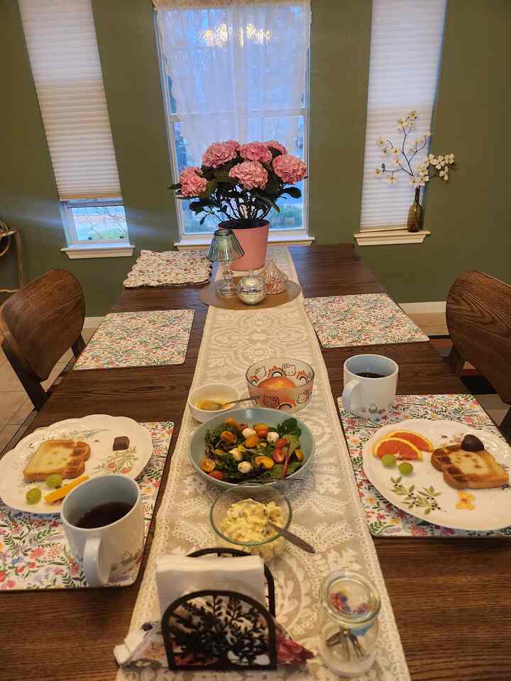 Green-walled dining room for four with white lace table runner, floral centerpiece, and cozy breakfast setting featuring coffee mugs