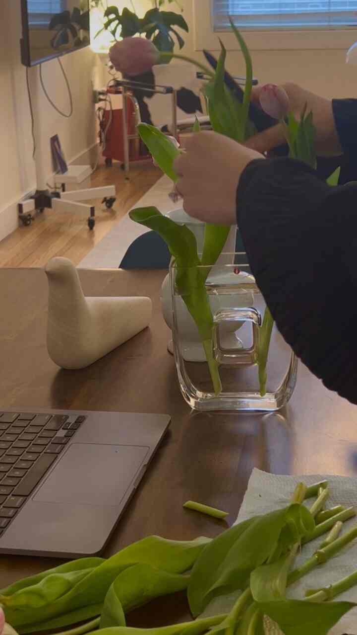 Natural home office space featuring pink tulips in a clear vase on a warm brown wooden table