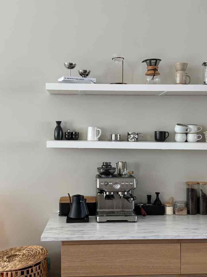 White and wood tone minimal Japandi style kitchen featuring a coffee machine and mugs, creating a cozy home cafe atmosphere