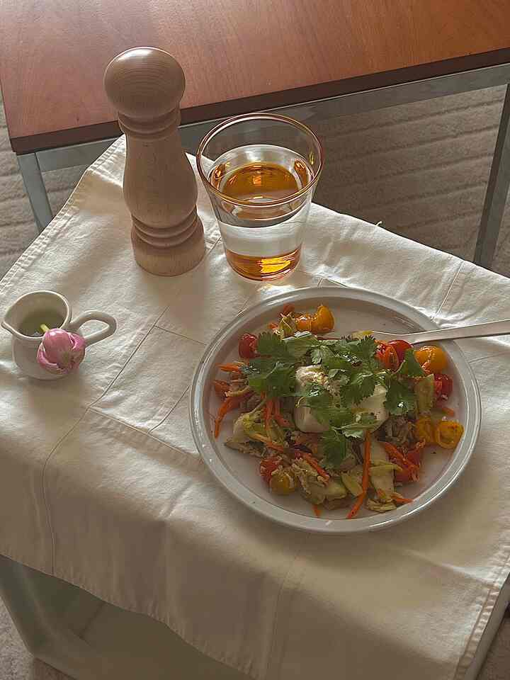Beige tablecloth and wood tone table featuring a plate of salad, glass, and wooden pepper mill on a cozy dining table setup