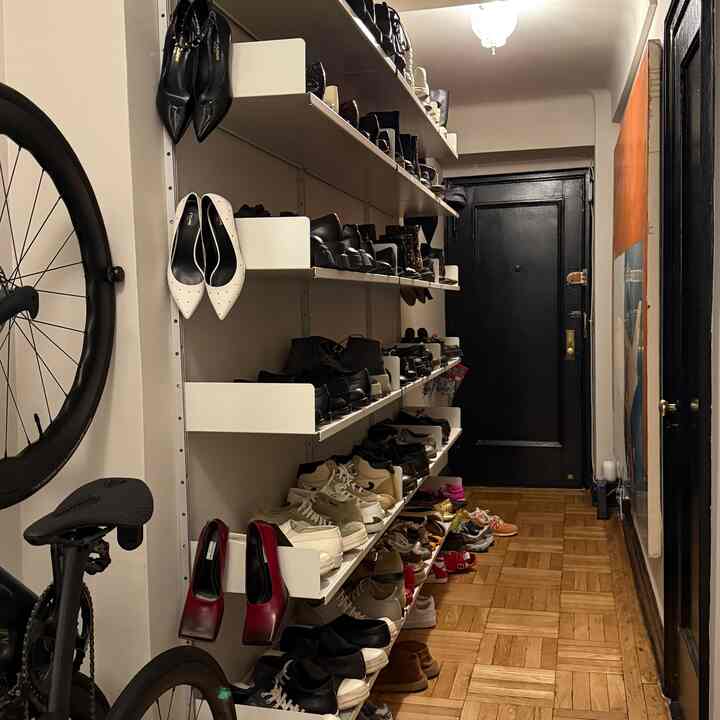 White and wood tone long narrow entrance featuring stylish Vitsoe shelving filled with shoes and a bicycle, presenting a minimal and modern space