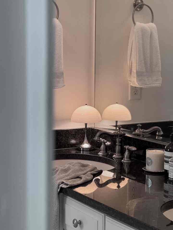 White and black toned bathroom featuring marble sink, table lamp, and candle creating cozy ambiance