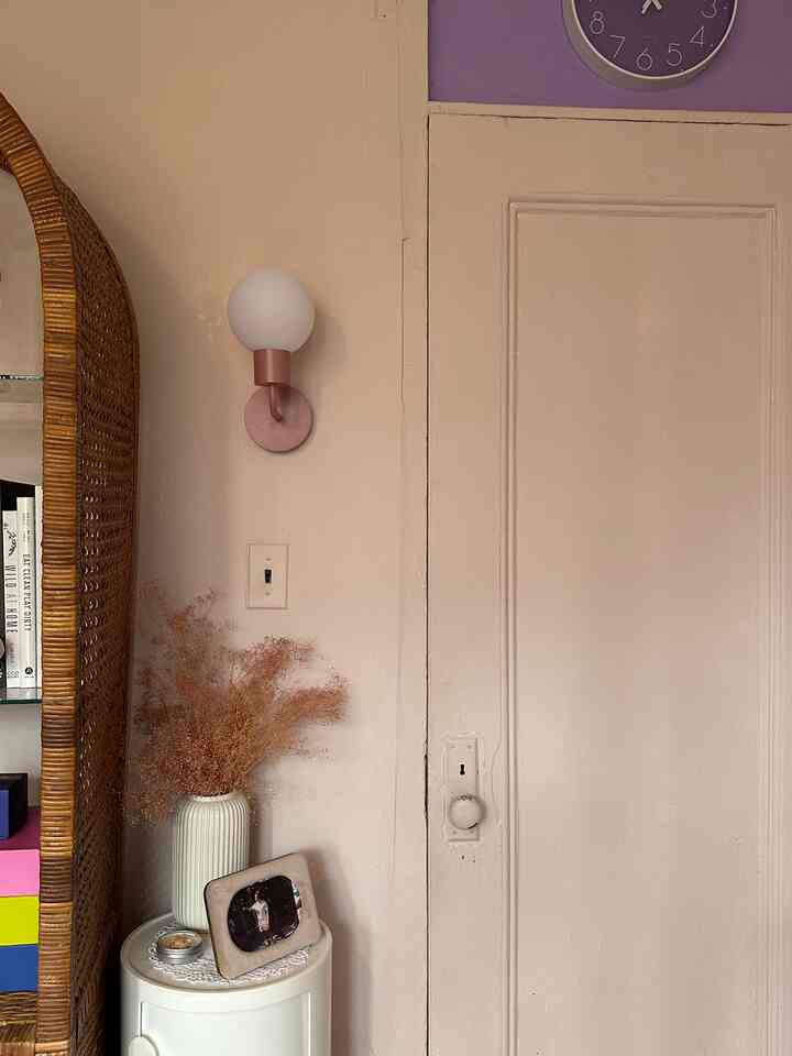 Beige-toned walls and door with wall sconce, rattan shelving, vase and picture frame creating a cozy vintage atmosphere