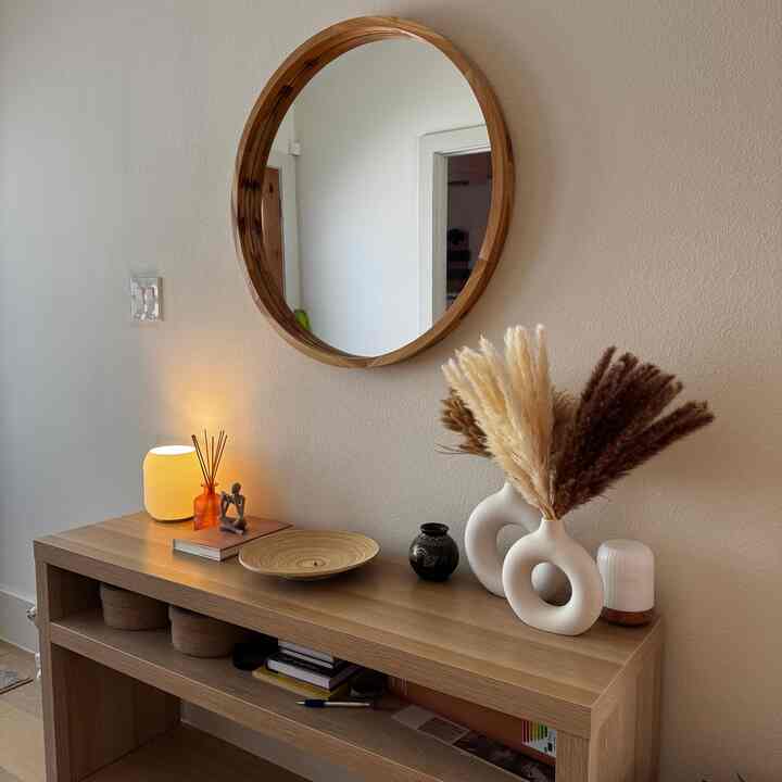 Wood tone and white entrance featuring a round wood framed mirror and console table with lamp and diffuser, creating a natural atmosphere