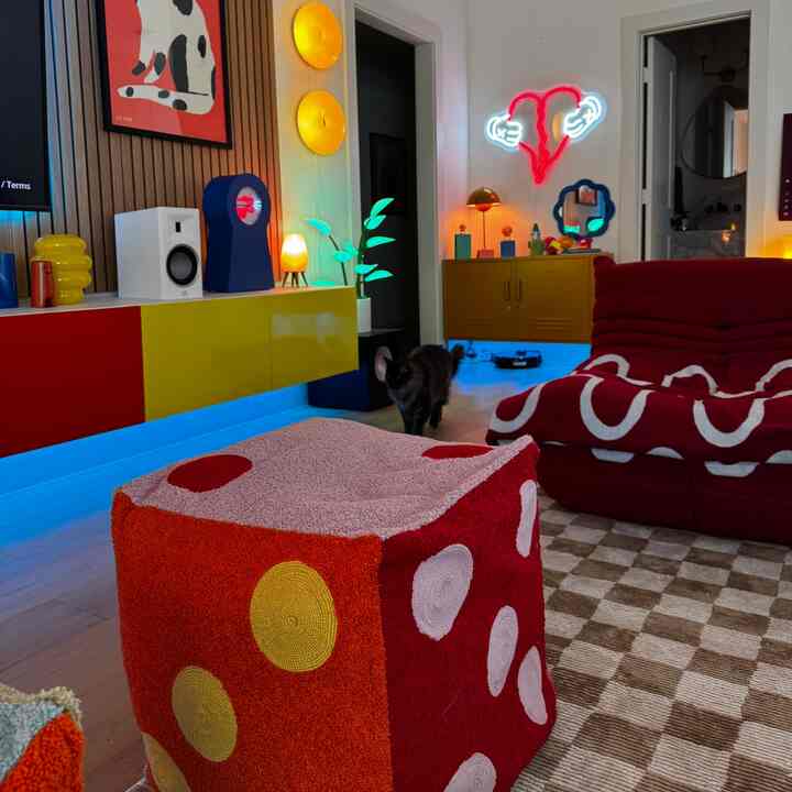 A red and yellow themed living room featuring colorful lighting, dice-shaped poufs, and a pet cat, creating a cozy atmosphere