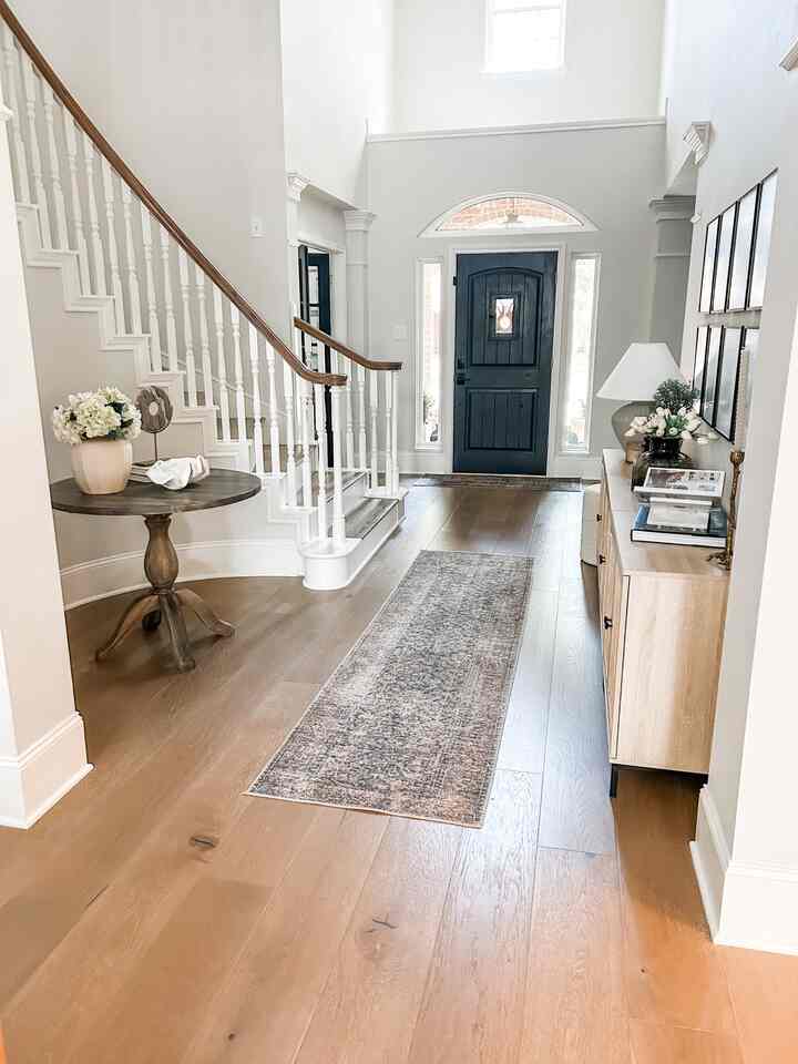 Natural-tone entrance with white walls and wood-tone flooring, featuring storage cabinet, round table, and gallery wall decor