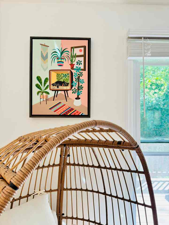 Bright and cozy living space with white walls, natural rattan chair, and framed cat artwork