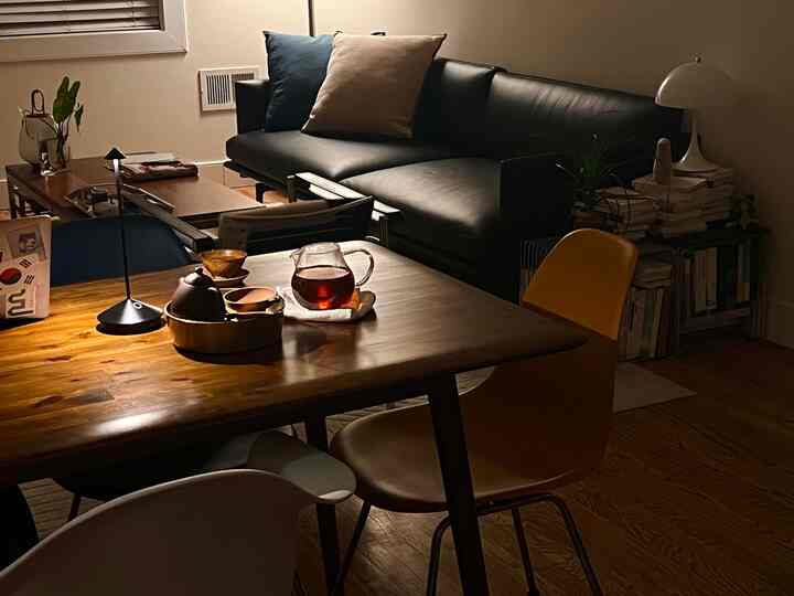 Natural living room with warm lighting featuring wooden dining table and black sofa