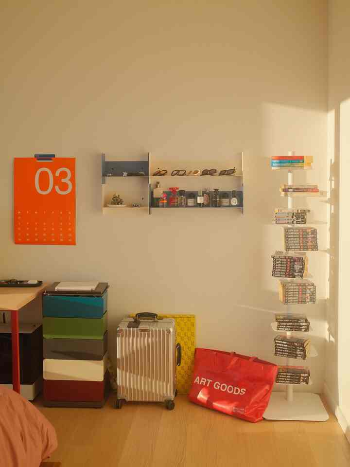 Natural wood-tone bedroom corner with red accent items, featuring wall shelves and bookshelf showcasing neat storage in a cozy space
