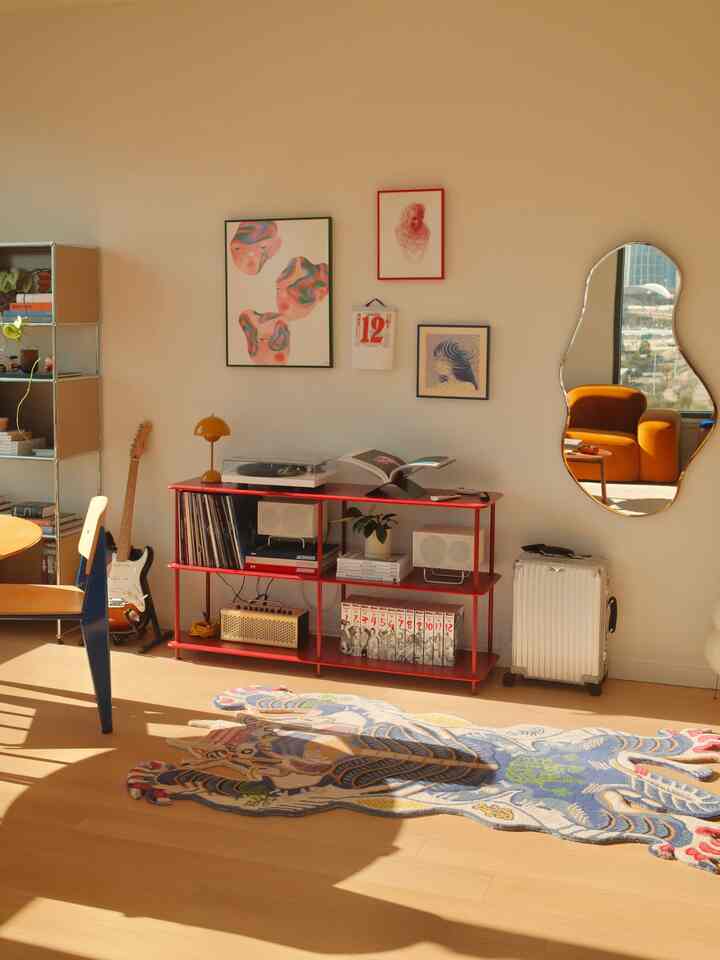 Warm brown floor and red shelving highlight this living room featuring a vintage-style sofa and diverse wall art in a cozy atmosphere