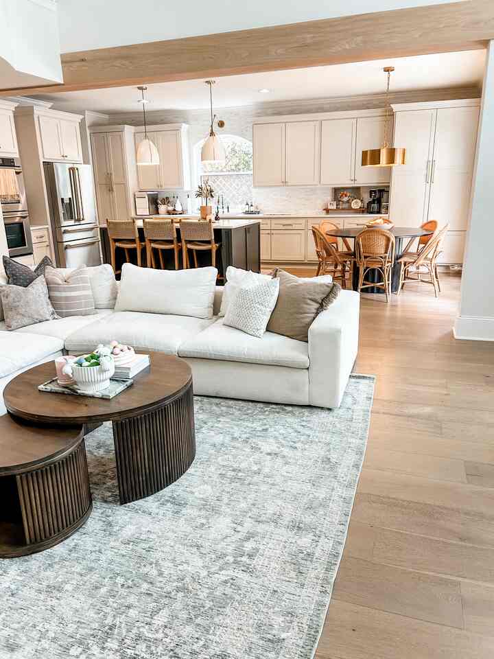 Natural color and wood tone open concept living room featuring a white sectional sofa, round coffee tables, and rattan dining chairs in a simple modern space