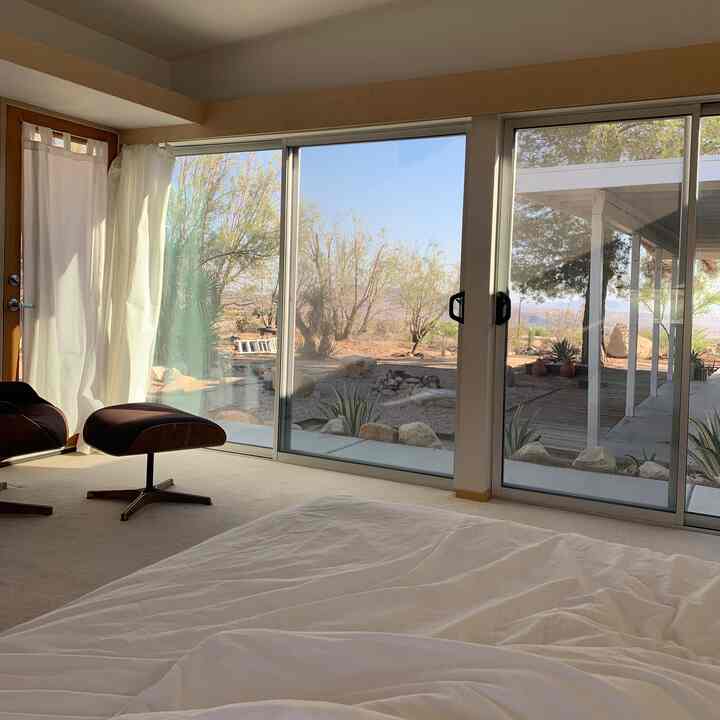 White and natural toned bedroom space featuring a black Eames Lounge Chair and white curtains, creating a modern atmosphere