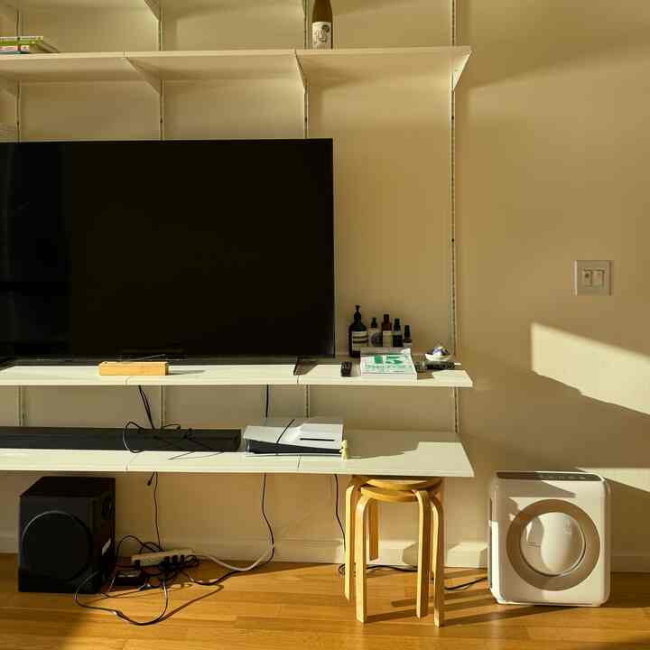 White and wood tone living room featuring TV, shelving and a stool with a simple and cozy atmosphere