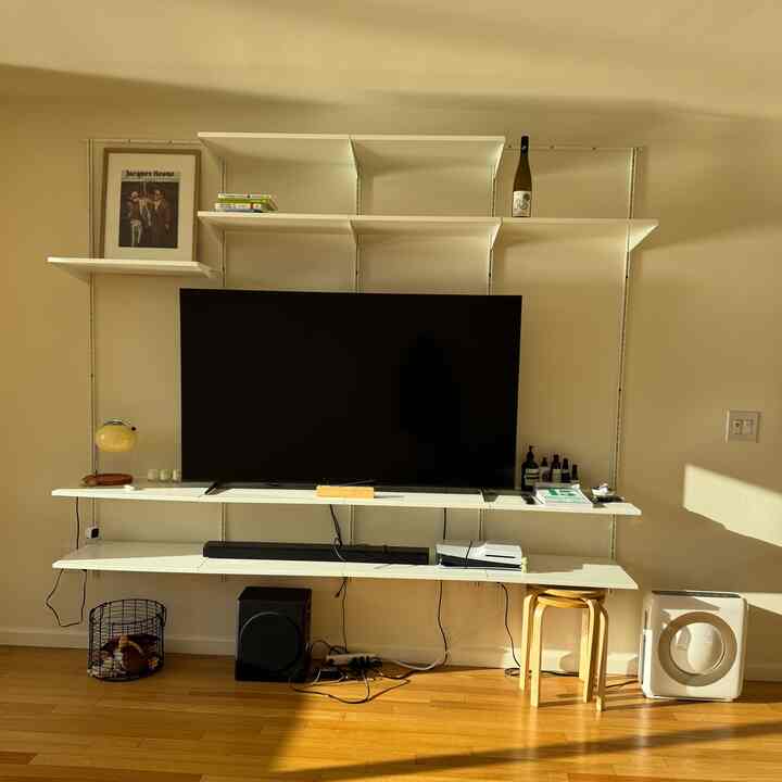 White shelves and brown wooden floor living room featuring a large TV with modular shelving for organized storage