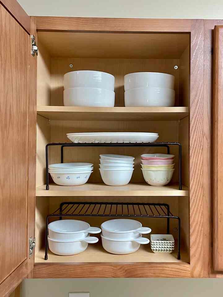 Minimalist kitchen cupboard in white and wood tones featuring organized bowls and clever storage ideas in a tidy space