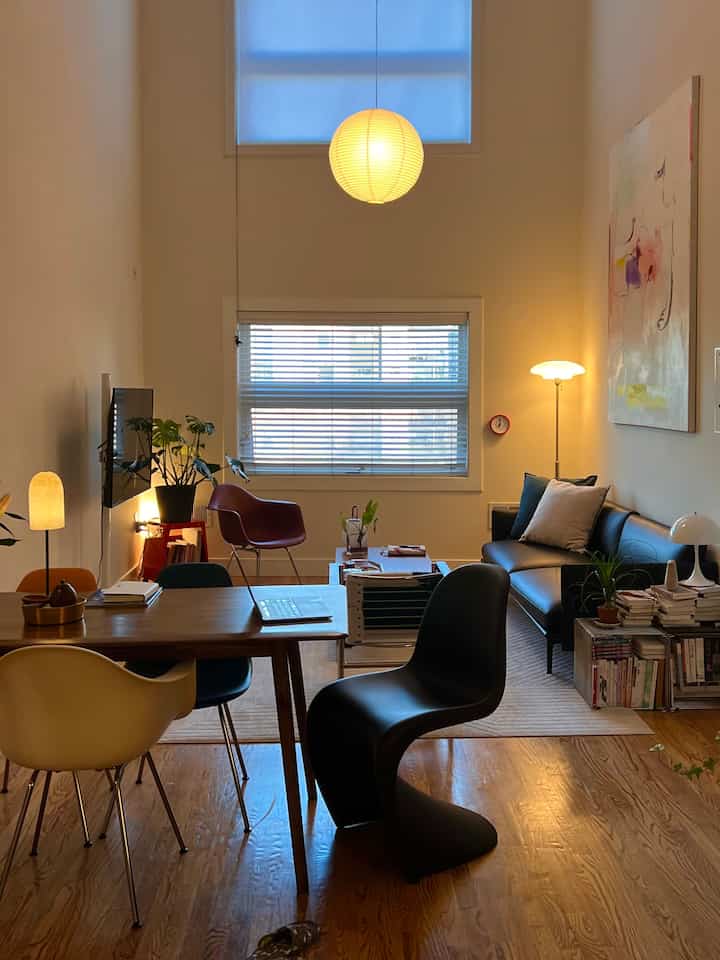 Warmly lit, wood-toned compact living and dining room featuring various chairs and sofa in a modern layout