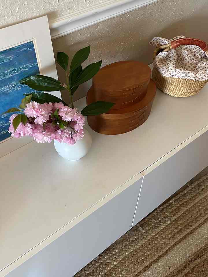 White cabinet surface topped with wood tone boxes and a vase with pink flowers, creating a neat entrance space