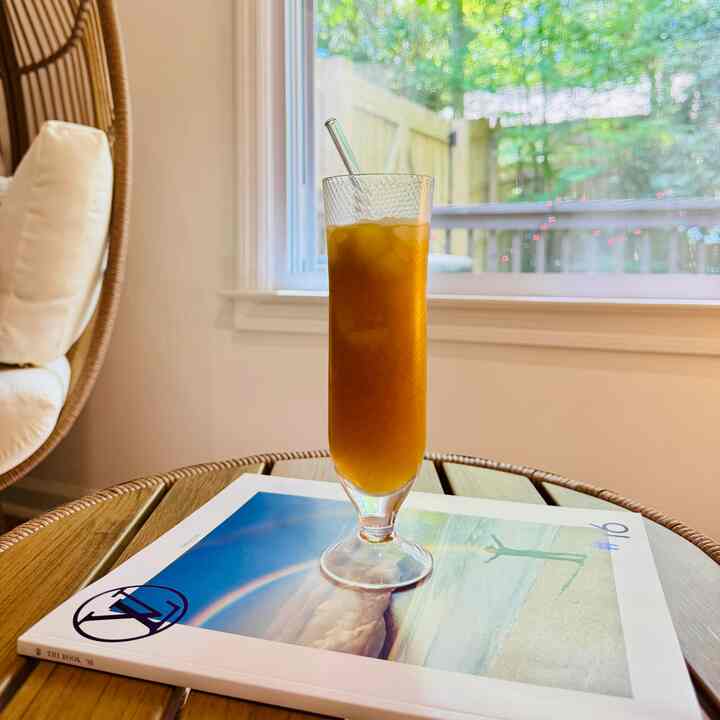 Wood tone side table featuring a glass of juice with transparent straw, bright spring sunlight fills the kitchen space