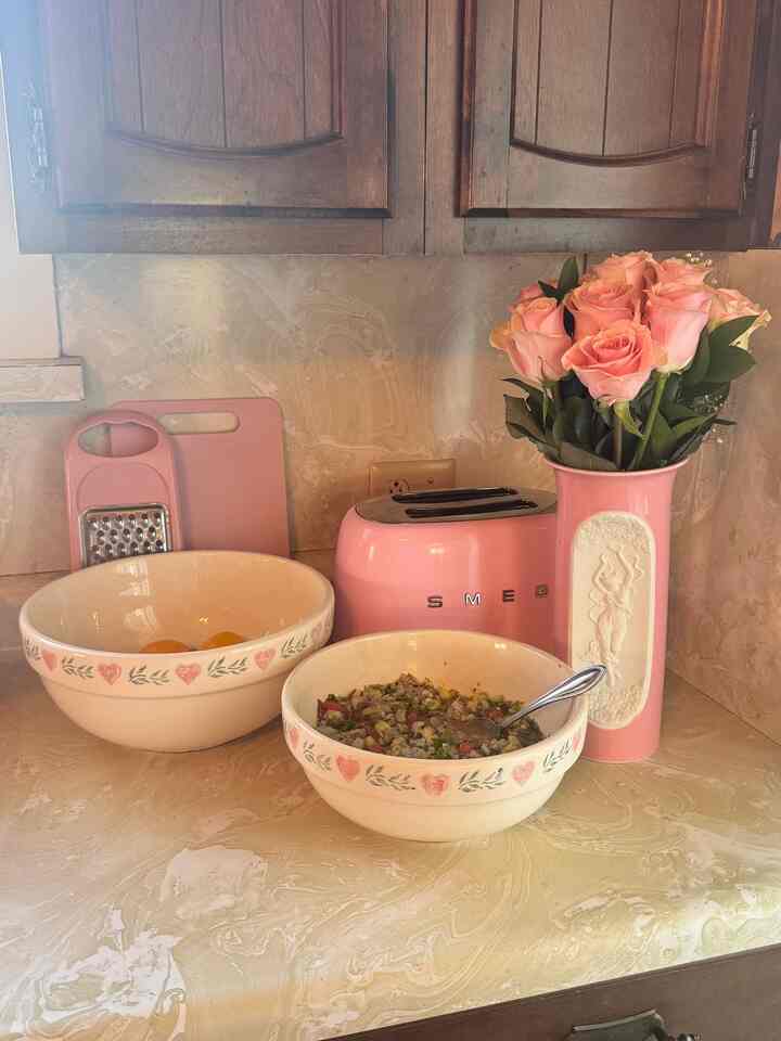 Pink-toned kitchen featuring a pink toaster, vase with roses, and heart-patterned bowls creating a warm vintage atmosphere