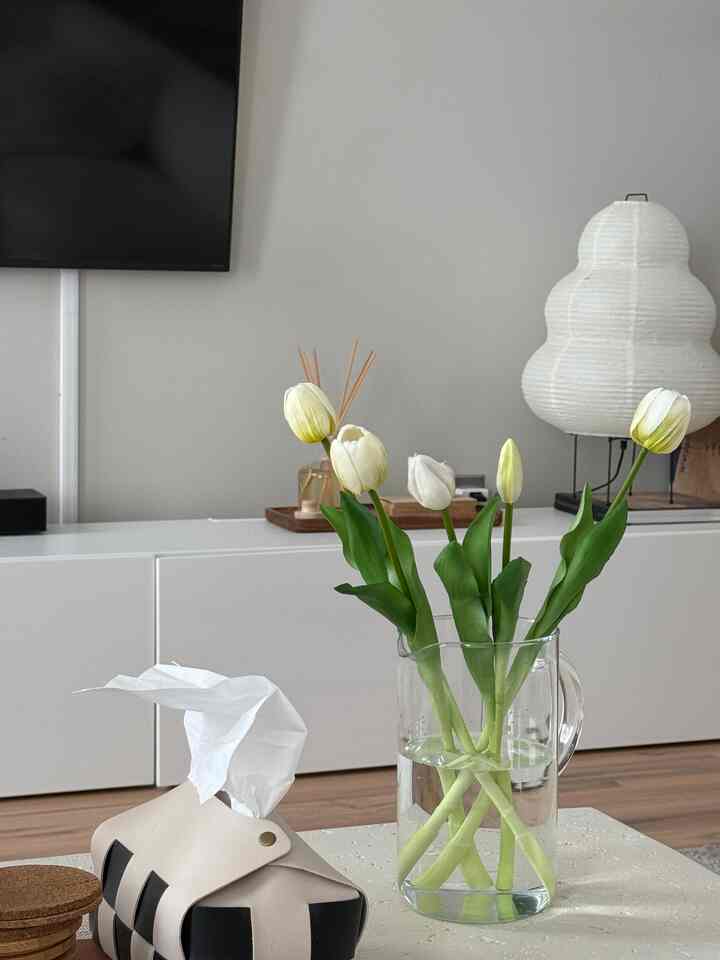 White and natural toned living room with transparent vase holding white tulips, presenting a simple and cozy atmosphere