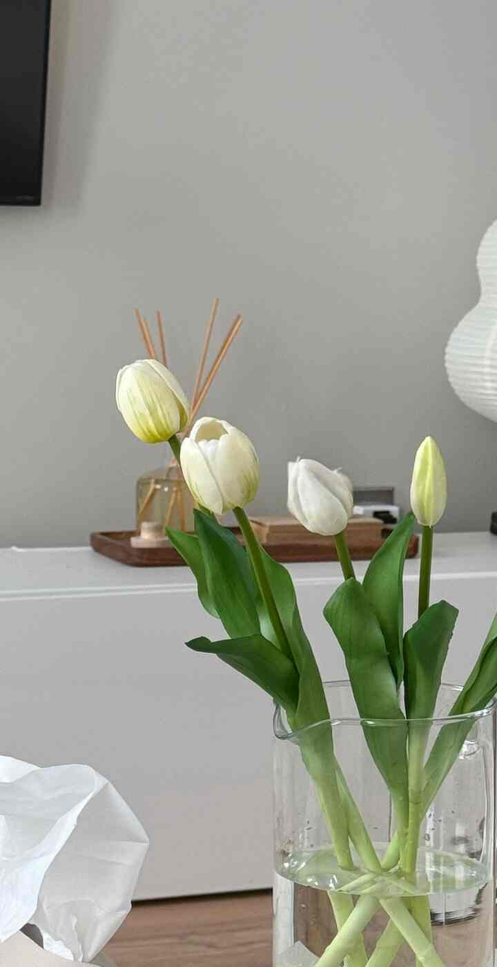 Soft gray walled living room with white furniture, featuring a clear vase with white tulip bouquet in a simple and natural setting