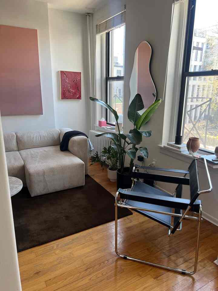 Modern living room with white walls and brown wooden floor, featuring a curved mirror and plants, creating a clean and cozy atmosphere