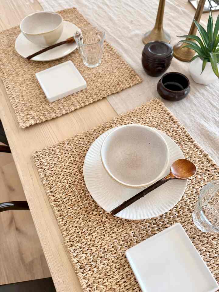Natural-toned dining room featuring a wooden dining table set with woven placemats and simple tableware